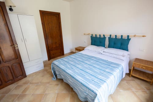 Camera luminosa nell'appartamento Emily, San Vito Lo Capo Sicilia con letto matrimoniale, cuscini blu, mobili in legno e pavimenti in piastrelle