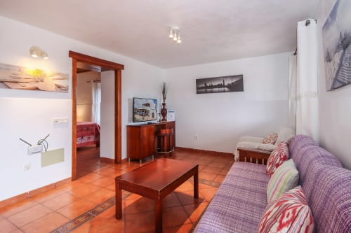 Amplio salón con pisos de terracota, sofá morado, muebles de madera y vistas a las montañas en Villanueva