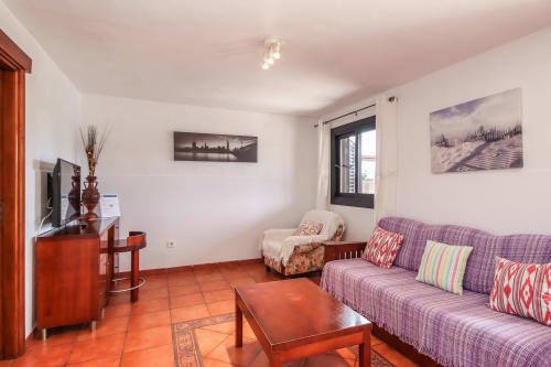 Amplio salón de apartamento en Villanueva Lanzarote con baldosas terracota, sofá morado, televisor y vistas a las montañas