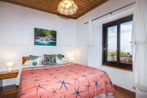 Habitación luminosa en Villanueva Lanzarote con ropa de cama de patrón coral, techo de madera, paredes blancas y vistas a las montañas