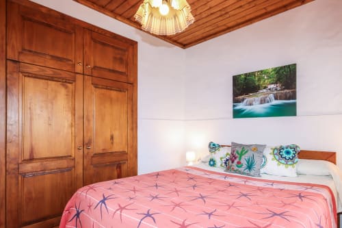 Dormitorio luminoso con armario de madera, colcha coral, almohadas coloridas y cuadro de cascada en Villanueva Lanzarote
