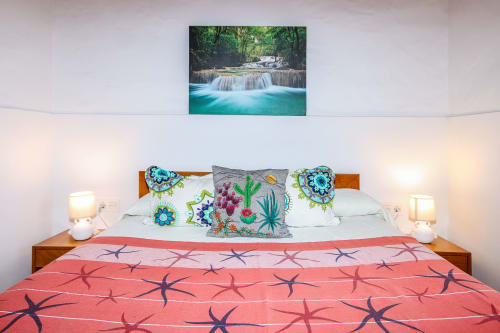 Dormitorio luminoso en Villanueva Lanzarote con ropa de cama colorida, marco de madera y arte de cascada sobre la cama en apartamento Mala