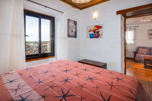 Dormitorio luminoso con ropa de cama estampada de estrellas de mar coral, vistas montañosas por ventana de marco negro, techo de madera y acceso