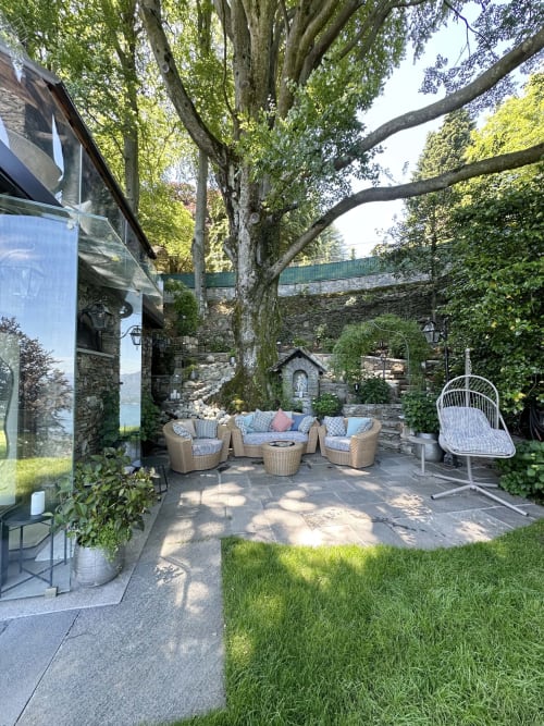 Luxury lakeside terrace with woven seating, stone walls, and mature trees overlooking Lake Maggiore, Stresa