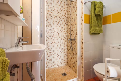 Baño moderno en apartamento de Villanueva Lanzarote con ducha de azulejos mosaico, lavamanos blanco, inodoro y toallas verde lima