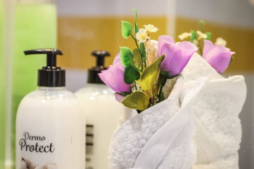 Amenidades spa en apartamento de Villanueva Lanzarote: toallas, flores y cosméticos Dermo Protect en el tocador del baño