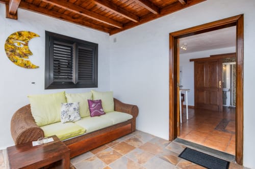 Acogedora sala de estar en apartamento de Villanueva Lanzarote con sofá de mimbre, cojines amarillos, vigas de madera y vistas a la montaña