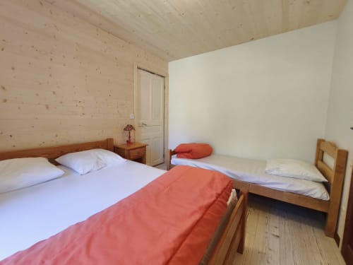 Chambre accueillante pour 3 personnes au Chalet Coste Belle à Ceillac avec lits en bois, draps blancs et touches rouges