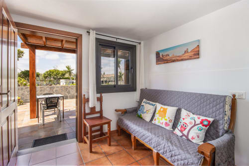 Salón luminoso en Lanzarote con sofá gris, cojines coloridos, acceso a terraza y vistas al jardín