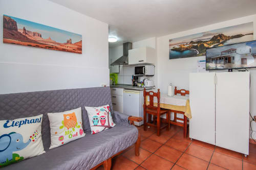 Acogedora sala de estar con sofá gris, cojines coloridos, cocineta, mesa de comedor de madera y piso de terracota