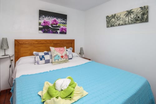 Dormitorio en Villanueva Lanzarote con cama de madera, manta azul, cojines decorativos y arte mural