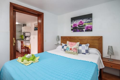 Dormitorio luminoso con colcha acolchada azul, cama de madera y vistas al jardín en el apartamento Villanueva Lanzarote en Mala