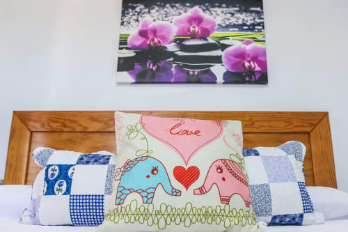 Dormitorio del apartamento Villanueva Lanzarote con cojín decorativo y cuadro de orquídea rosa sobre cabecero de madera