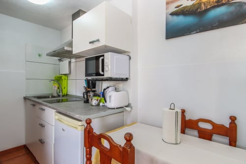 Cocina compacta en apartamento de Villanueva Lanzarote con muebles blancos, microondas, estufa y sillas de madera