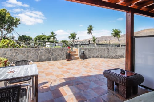 Amplia terraza del apartamento Villanueva Lanzarote con vistas al jardín, muebles de mimbre y paisaje montañoso en Mala