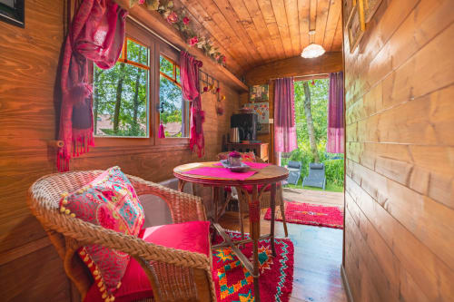 Intérieur douillet de roulotte aux Gîtes du Rouard à Camiers : accents rose, murs en bois, chaises en osier et vue sur le jardin