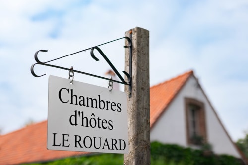 Enseigne Chambres d'hôtes LE ROUARD à Camiers avec bâtiment et toit en terre cuite en arrière-plan