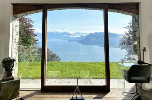 Studio di lusso con vista panoramica sul Lago Maggiore, terrazze verdi e montagne alpine visibili attraverso finestre a tutta altezza