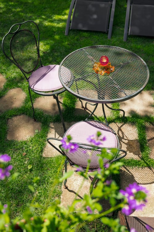 Salon de jardin en métal avec table et chaises à mailles aux Gîtes du Rouard à Camiers, entouré de fleurs violettes et pelouse verte