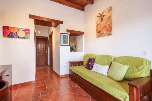 Luminoso salón con sofá verde lima, suelos de baldosa terracota y vigas de madera en apartamento Villanueva Lanzarote en Mala,