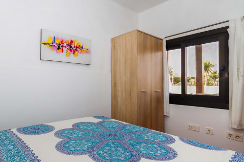 Dormitorio luminoso en Villanueva Lanzarote con ropa de cama turquesa estampada, armario de madera, arte colorido en la pared y vistas a montaña