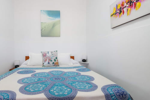 Habitación en Villanueva Lanzarote con ropa de cama turquesa estampada, almohadas blancas, obra de arte paisajística y arte mural colorido