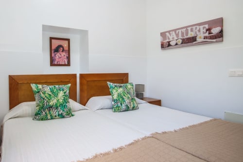 Dormitorio moderno con camas gemelas, almohadas con hojas verdes y vistas a las montañas en el apartamento Villanueva Lanzarote en Mala