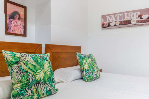 Dormitorio luminoso con cabecero de madera, almohadas con patrón tropical verde, ropa de cama blanca y arte mural en Villanueva Lanzarote