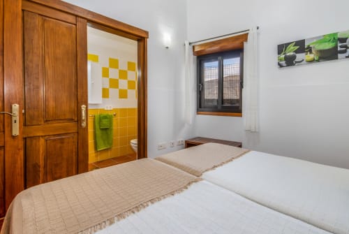 Luminosa habitación con dos camas, puerta de madera, baño con azulejos amarillos y vistas a la montaña en Villanueva Lanzarote, Mala