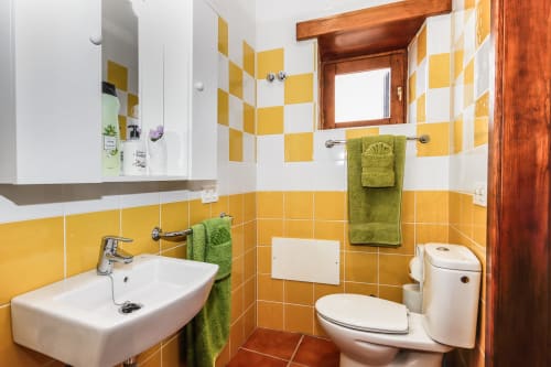 Baño luminoso con azulejos amarillo y blanco en Villanueva Lanzarote, lavabo, inodoro y toallas verdes
