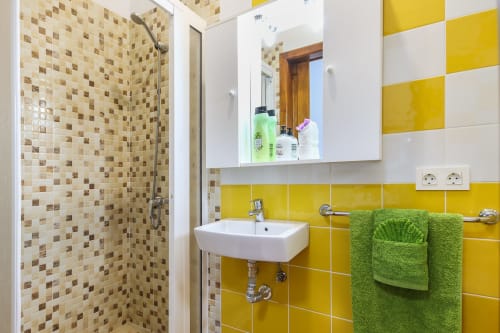 Baño moderno en Villanueva Lanzarote con azulejos amarillos, ducha de mosaico, lavabo blanco, toallas verdes y botiquín espejo