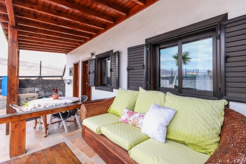 Terraza de apartamento en Villanueva, Lanzarote con sofá verde lima, vigas de madera, vistas a la montaña y ventanales negros en Mala