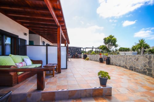 Amplia terraza en Villanueva Lanzarote con pérgola de madera, zona de descanso, plantas en macetas y vistas a las montañas en Mala