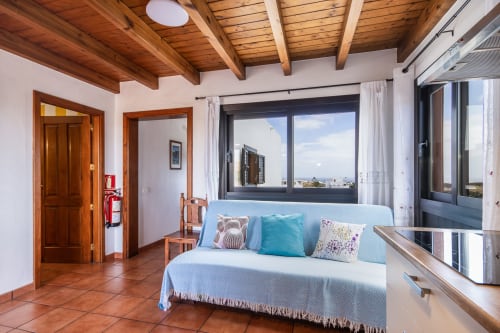 Luminosa habitación de apartamento superior en Villanueva Lanzarote con techo de vigas de madera, ropa de cama azul, amplias ventanas y vistas al mar