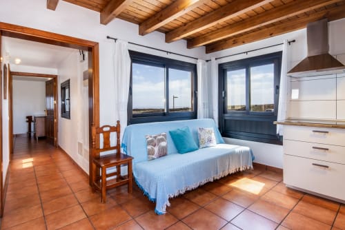 Luminoso apartamento superior en Villanueva Lanzarote con sofá azul, vigas de madera, suelos de terracota y vistas panorámicas al mar