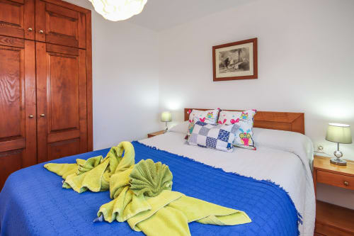 Dormitorio del apartamento en Villanueva Lanzarote con muebles de madera, manta azul, almohadas coloridas y ropa de cama blanca