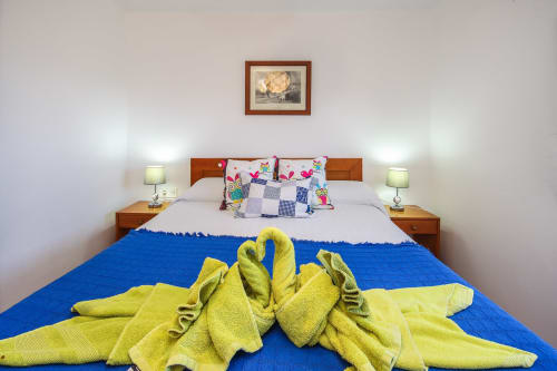 Dormitorio espacioso en Villanueva Lanzarote con cama de madera, almohadas coloridas, toallas amarillas, lámparas de noche y cuadros enmarcados.