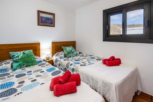 Luminoso dormitorio doble en Villanueva Lanzarote con camas de madera, almohadas coloridas, toallas rojas y vistas al mar