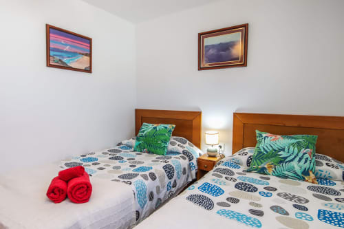 Camas gemelas con almohadas coloridas y toallas rojas en apartamento de Villanueva Lanzarote, cuadros de paisajes en las paredes