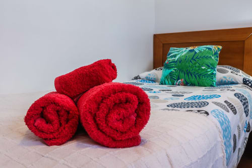 Toallas rojas enrolladas en la cama con almohada tropical en el apartamento Villanueva Lanzarote de Mala, Islas Canarias