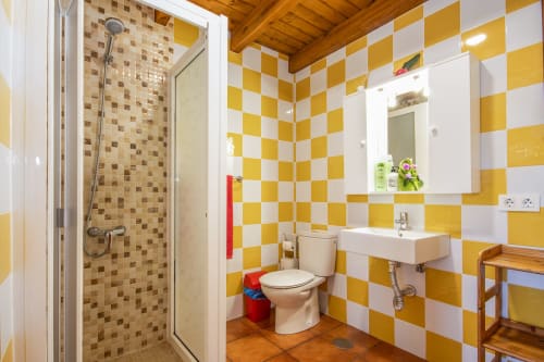 Baño luminoso en Villanueva Lanzarote con paredes de cuadros amarillos y blancos, accesorios modernos y ducha