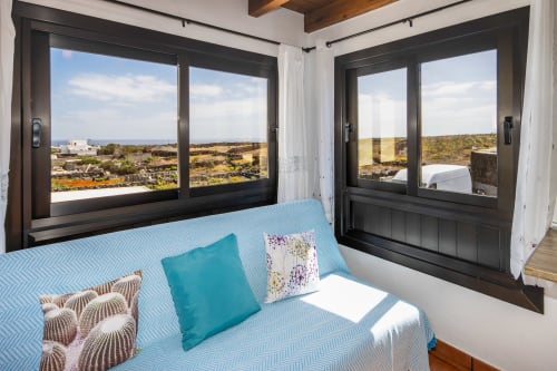 Dormitorio moderno con vistas al mar en Villanueva Lanzarote, con ropa de cama azul y ventanas de marco negro con vista a Lanzarote