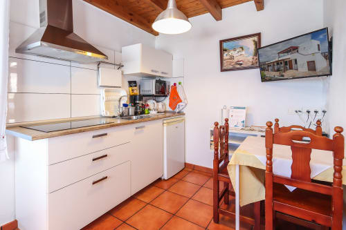 Cocina y comedor moderno con muebles blancos, vigas de madera, baldosas de terracota y sillas rojas de madera en Villanueva