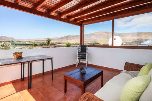 Terraza cubierta en Villanueva Lanzarote con mesa de comedor, mesa de café azul y vistas panorámicas a las montañas en Mala, Lanzarote