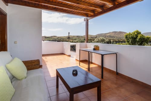 Amplia terraza en Villanueva Lanzarote con asientos, mesa de comedor, pérgola de madera y vistas panorámicas a las montañas