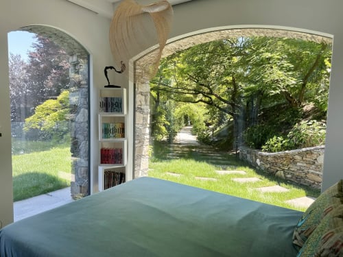 Luxury bedroom with panoramic lake view, garden access, bookshelf, and woven pendant lamp in Stresa, Italy