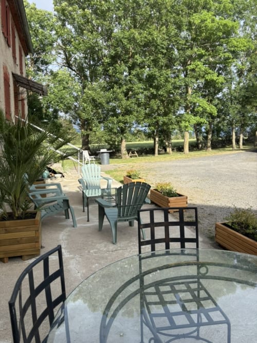 Espace de détente extérieur du Mas De Bannayoux avec chaises Adirondack, foyer et terrain bordé d'arbres à Couteuges.