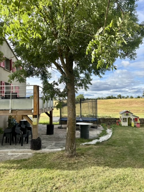 Terrasse extérieure du Mas De Bannayoux avec grand arbre, coin repas, trampoline et vue sur la campagne à Couteuges, France