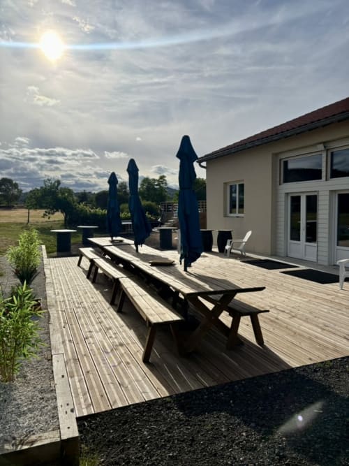 Salle de réception extérieure au Mas De Bannayoux avec terrasse en bois, tables de restauration, parasols bleus et vue sur les montagnes à Couteuges,