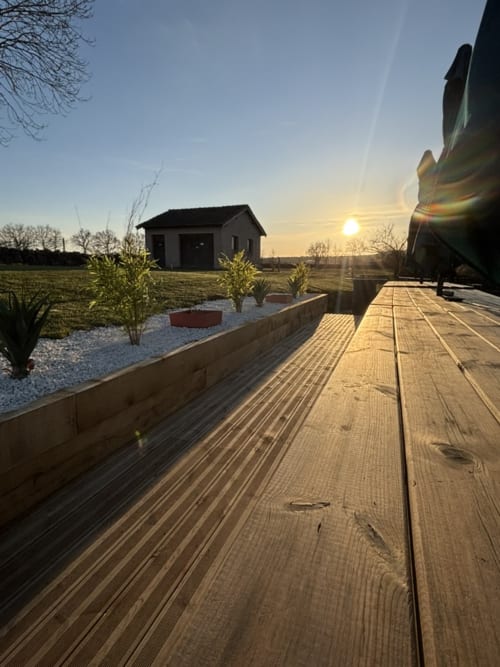 Terrasse en bois de la salle de réception Mas De Bannayoux surplombant les champs au coucher de soleil et une petite maison à Couteuges